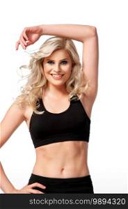 Portrait of a smiling fit young white female athlete with curly long blond hair posing by herself in a studio with a white background wearing black shorts   sports bra.
