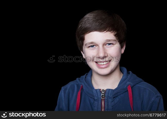 Portrait of a smiling fourteen year old boy on a black background.