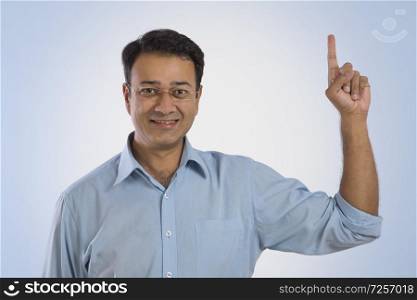 Portrait of a smiling man in eyeglasses standing with his index finger pointing upwards