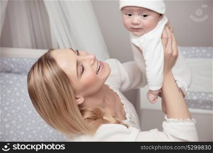 Portrait of a smiling mother with her precious baby spending time at home, enjoying parenting, happy family life