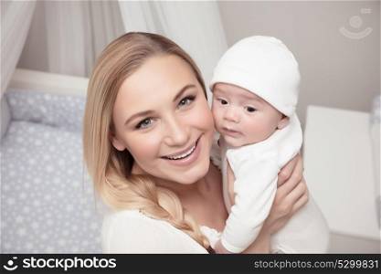 Portrait of a smiling mother with her precious baby spending time at home, enjoying parenting, happy family life