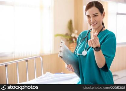 Portrait of a smiling nurse or medical staff make a mini heart hand sign in a hospital, happy woman doctor in uniform holding clipboard, people medical healthcare concept
