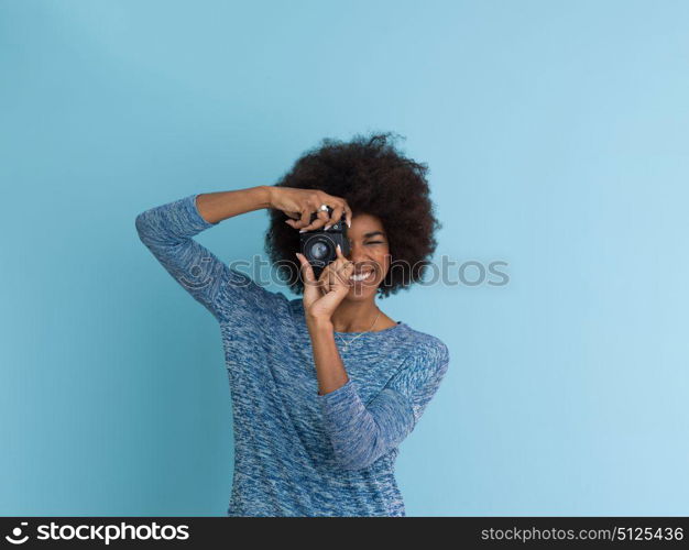 portrait of a smiling pretty african american girl taking photo on a retro camera isolated over blue background