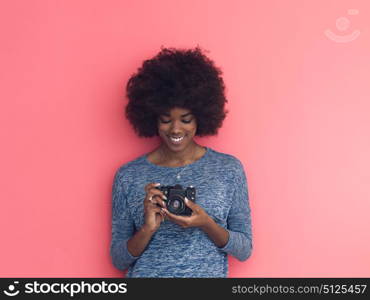 portrait of a smiling pretty african american girl taking photo on a retro camera isolated over pink background