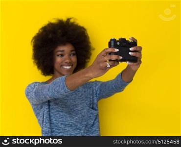 portrait of a smiling pretty african american girl taking photo on a retro camera isolated over yellow background