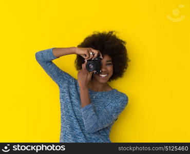 portrait of a smiling pretty african american girl taking photo on a retro camera isolated over yellow background