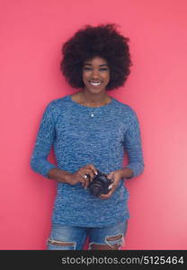 portrait of a smiling pretty african american girl taking photo on a retro camera isolated over pink background