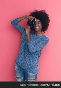 portrait of a smiling pretty african american girl taking photo on a retro camera isolated over pink background