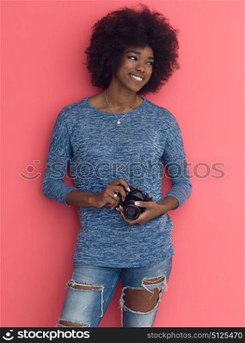 portrait of a smiling pretty african american girl taking photo on a retro camera isolated over pink background