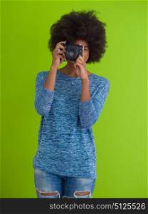 portrait of a smiling pretty african american girl taking photo on a retro camera isolated over green background