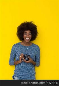 portrait of a smiling pretty african american girl taking photo on a retro camera isolated over yellow background