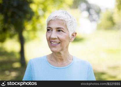 Portrait of a smiling sporty senior woman in a park at summer day