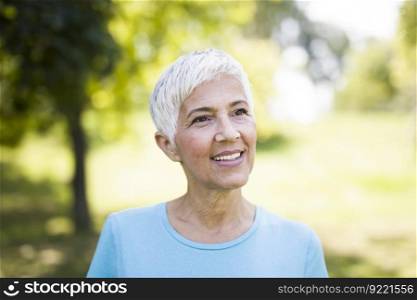 Portrait of a smiling sporty senior woman in a park at summer day