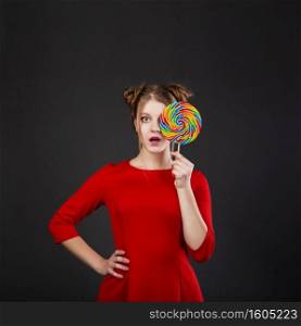 Portrait of a smiling young beautiful girl in a red dress with a big candy. Funny girl with a lollipop