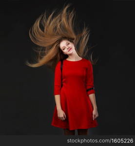 Portrait of a smiling young beautiful girl in a red dress with a flying hair. Girl with long flowing hair. Hair fluttering in motion.
