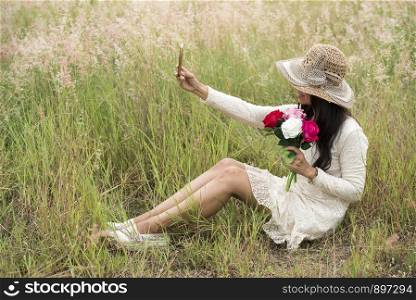 Portrait of a smiling young beautiful woman wear hat with a bouquet of roses flowers. Outdoors with a grasses meadow.