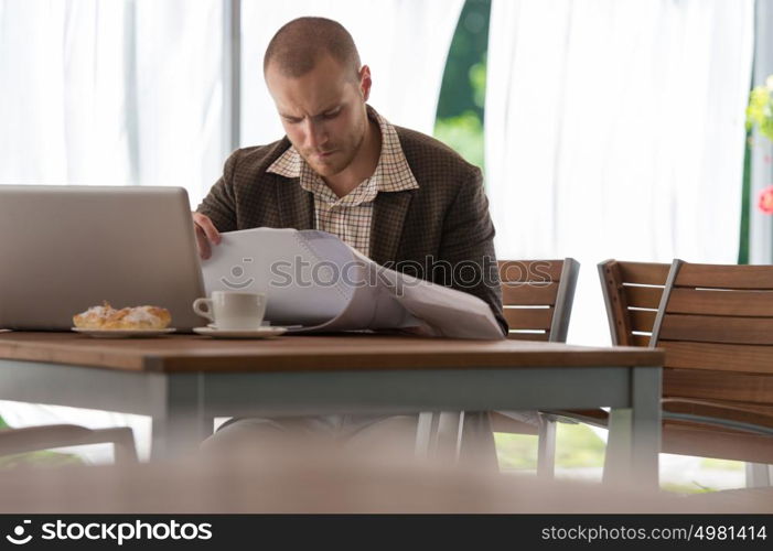 Portrait of a smiling young businessman working with blueprints at the cafe