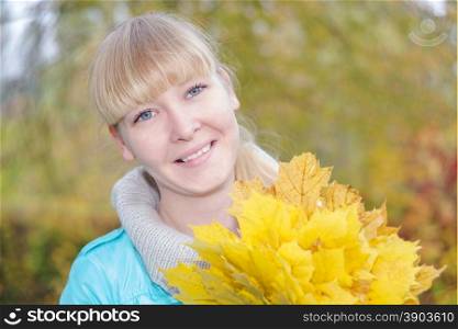 Portrait of a smiling young girl with bouquet of yellow maple leaf in the autumn nature looking at the camera