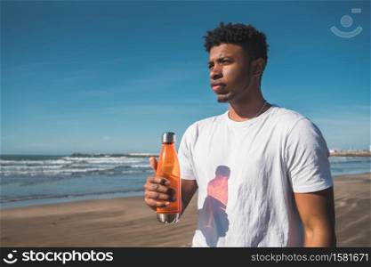 Portrait of a sport man holding a bottle of water at the beach. Sport and health lifestyle.