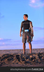 Portrait of a strong young surf man at beach on sunset in a contemplative mood with a surfboard