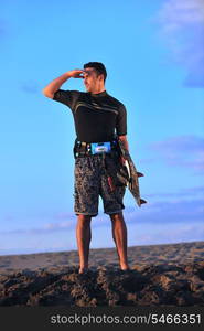 Portrait of a strong young surf man at beach on sunset in a contemplative mood with a surfboard