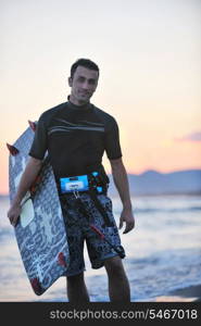 Portrait of a strong young surf man at beach on sunset in a contemplative mood with a surfboard