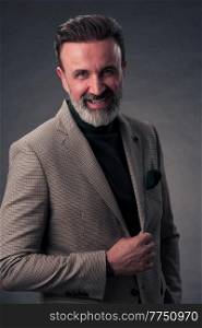Portrait of a stylish elegant senior businessman with a beard and casual business clothes in photo studio isolated on dark background gesturing with hands. High quality photo. Portrait of a stylish elegant senior businessman with a beard and casual business clothes in photo studio isolated on dark background gesturing with hands