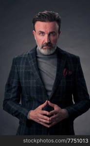 Portrait of a stylish elegant senior businessman with a beard and casual business clothes in photo studio isolated on dark background gesturing with hands. High quality photo. Portrait of a stylish elegant senior businessman with a beard and casual business clothes in photo studio isolated on dark background gesturing with hands