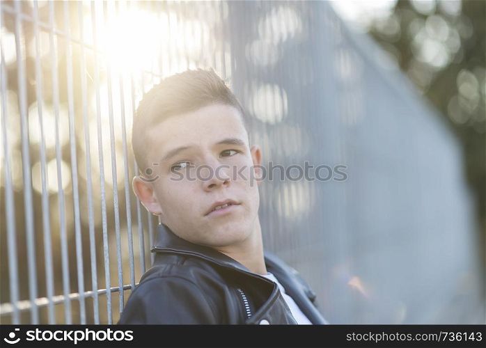 Portrait of a stylish teenager standing against a fence on a city park
