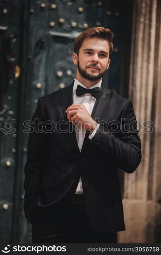 portrait of a stylish young groom in an old European town. man in a stylish suit with bow tie near old building. wedding day.. portrait of a stylish young groom in an old European town. man in a stylish suit with bow tie near old building. wedding day