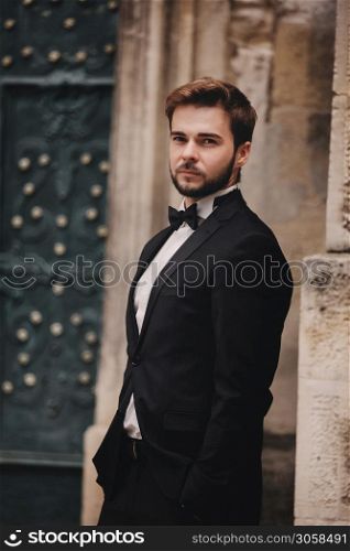 portrait of a stylish young groom in an old European town. man in a stylish suit with bow tie near old building. wedding day.. portrait of a stylish young groom in an old European town. man in a stylish suit with bow tie near old building. wedding day