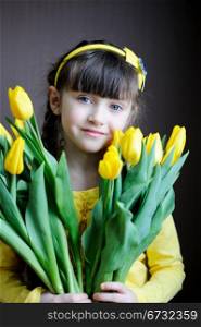 Portrait of a sunny child girl with bouquet of yellow tulips on a dark background