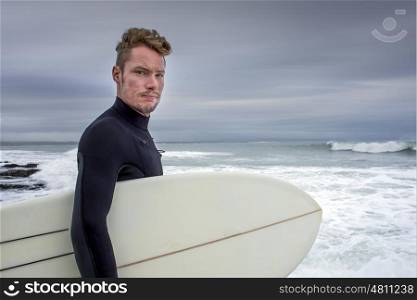 "Portrait of a surfer with his surfboard under his arm as he stands by the beach at "The Point" in Jeffreys Bay."