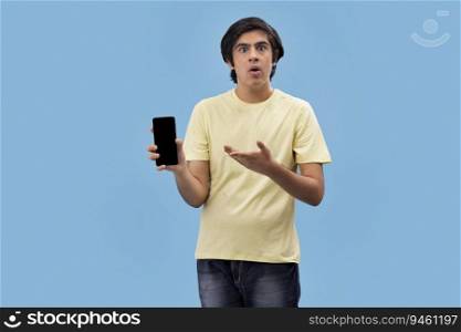 Portrait of a surprised teenage boy holding a Smartphone and gesturing against blue background