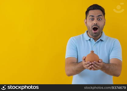 Portrait of a surprised young man standing with a clay saving pot in his hand against yellow background 