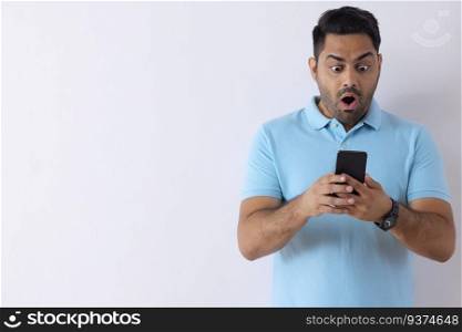 Portrait of a surprised young man standing with Smartphone against white background