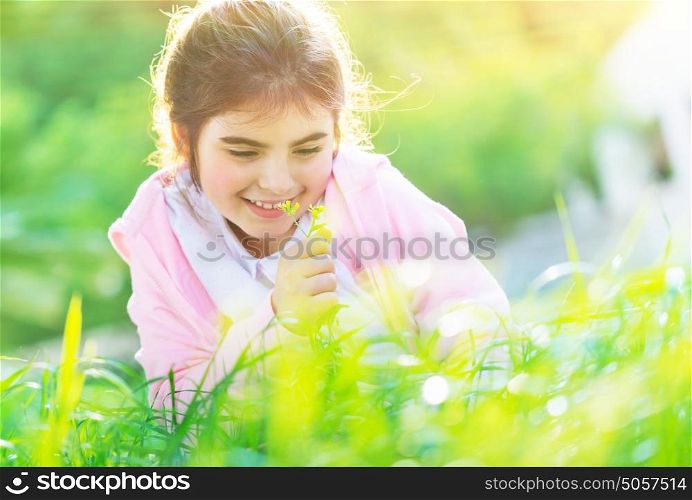 Portrait of a sweet baby girl sitting on the fresh green grass field and enjoying aroma of flowers, happy spring holidays in countryside