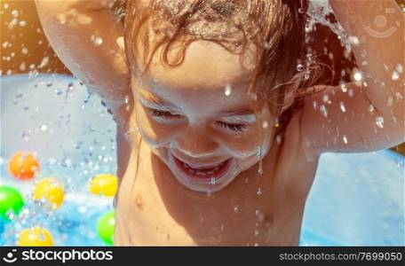Portrait of a sweet little boy enjoying warm water splashes, spending bright hot sunny day in the pool in aquapark, summer holidays on the beach resort, happy healthy childhood
