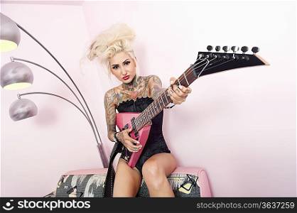 Portrait of a tattooed woman wearing corset while holding guitar against wall