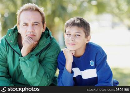 Portrait of a teenage boy and his father sitting with their hands on their chins