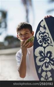 Portrait of a teenage boy eating a slice of watermelon and holding a body board