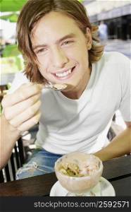 Portrait of a teenage boy eating an ice-cream sundae and smiling