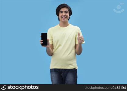 Portrait of a teenage boy holding a Smartphone and gesturing while standing against blue background