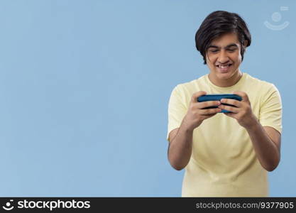 Portrait of a teenage boy playing games on Smartphone while standing against blue background