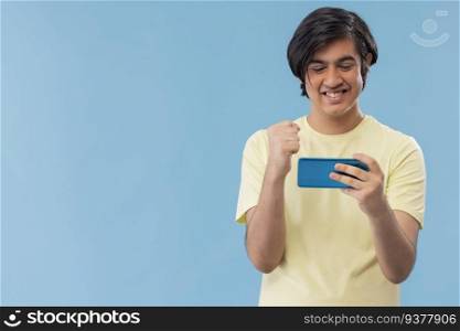 Portrait of a teenage boy playing games on Smartphone while standing against blue background