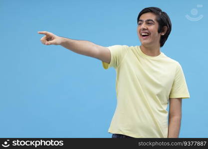Portrait of a teenage boy pointing away against blue background