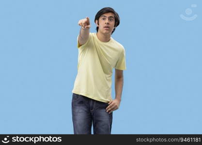 Portrait of a teenage boy pointing away while standing against blue background