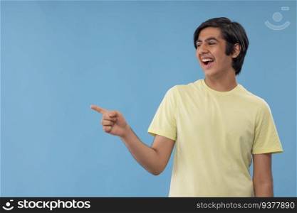 Portrait of a teenage boy pointing sideways against blue background