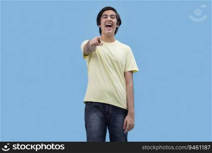 Portrait of a teenage boy pointing towards camera while standing against blue background