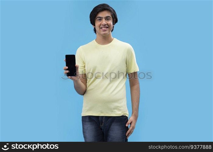 Portrait of a teenage boy showing Smartphone while standing against blue background